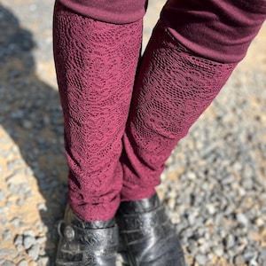 May include: Burgundy leggings with a lace pattern. The leggings are folded over at the top, showing a solid burgundy fabric. The leggings are worn with black leather shoes.