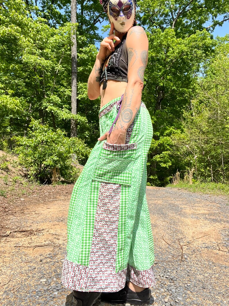 May include: Green and white checkered pants with a brown and white patterned panel on the side. The pants have a large pocket on the side and a ruffle at the bottom.