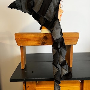 Pode incluir: Um chapéu de patchwork preto e cinza com uma longa cauda em espiral. O chapéu é feito de várias peças de tecido costuradas, criando uma aparência texturizada. É exibido em uma cabeça de manequim.