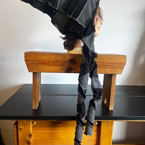 May include: A black and gray patchwork hat with a long, spiraling scarf. The hat is made of various fabric squares and has a pointed tip. The scarf is attached to the hat and hangs down, adding a unique flair to the design.