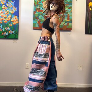 May include: A black halter crop top paired with wide-leg pants featuring a patchwork design of solid blue denim, solid pink fabric, and horizontal striped panels in pink, white, and blue. The pants include a tie-waist detail and black boots.