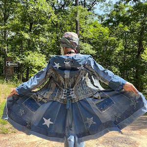 Puede incluir: Una chaqueta vaquera con un diseño de estrellas y una espalda estilo corsé. La chaqueta está hecha de varias piezas de mezclilla cosidas juntas y presenta una estrella blanca en la espalda con el texto "Feel The Energy".