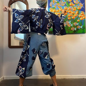 May include: Navy blue kimono-style top and denim pants set. The top features white leaf designs. The denim pants have patches of various shapes and sizes. The outfit is paired with black shoes. The background includes a mirror and a colorful painting.