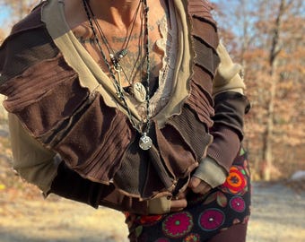 May include: A person wearing a brown and beige layered top with a ruffled neckline. They are wearing a black and red skirt with a floral pattern and burgundy leggings. The person is also wearing a white mask with purple accents and multiple necklaces.