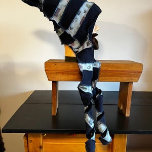 May include: A whimsical, dark blue hat with a long, spiraling tail. The hat features alternating stripes of solid blue and patterned fabric with small, repeating designs. The tail is also spiraled and patterned, creating a unique, playful accessory.