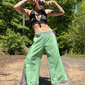 May include: A person wearing a green and white checkered pants with a black halter top and a black and white polka dot bandana. The person is wearing a mask with a butterfly design.