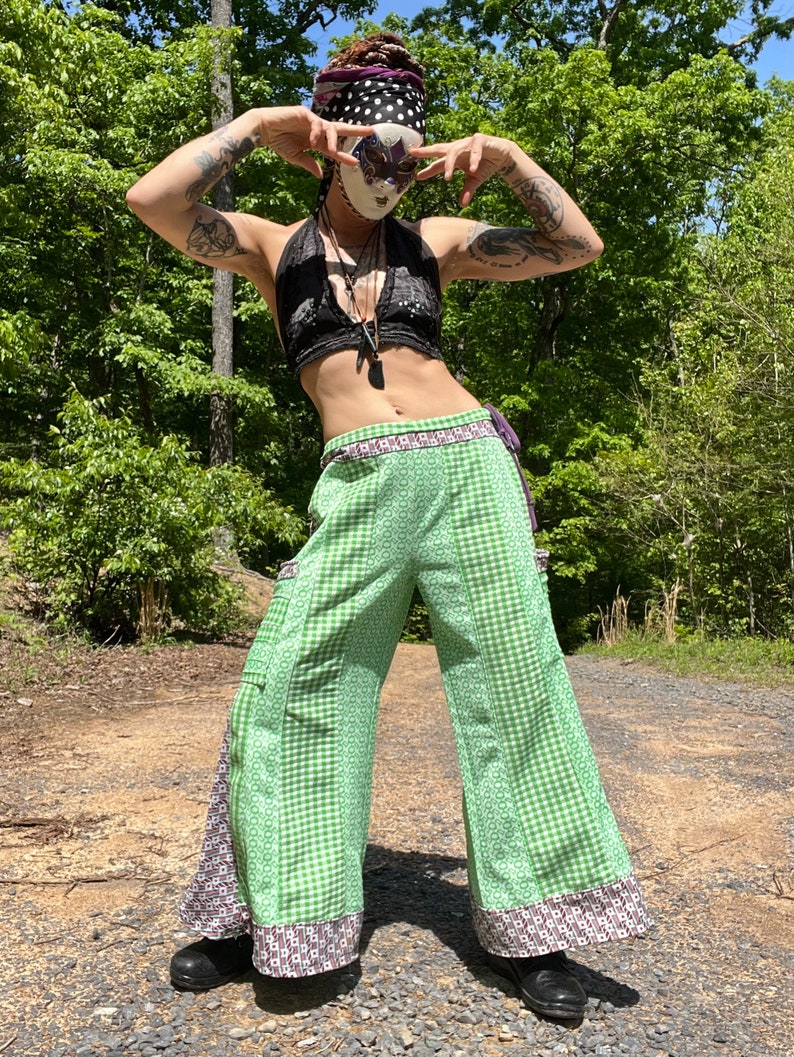 May include: A person wearing a green and white checkered pants with a black halter top and a black and white polka dot bandana. The person is wearing a mask with a butterfly design.