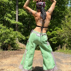 May include: A person wearing green and white checkered pants with brown and white trim. The pants have large pockets on the sides. The person is wearing a black bra and a black and white polka dot bandana on their head.