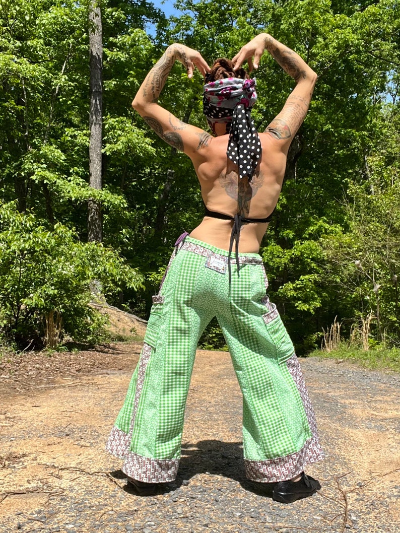 May include: A person wearing green and white checkered pants with brown and white trim. The pants have large pockets on the sides. The person is wearing a black bra and a black and white polka dot bandana on their head.