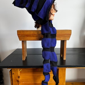 May include: A handmade, striped hat and scarf set in black and royal blue. The hat has a pointed top and the scarf is long and twisted. The set is made of a soft, textured fabric, perfect for cosplay or costume events.