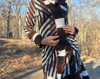 May include: A long brown and white striped cardigan with a ruffled hem and a belt. The cardigan is made of a soft, knitted fabric and has a relaxed fit. The model is wearing a masquerade mask.