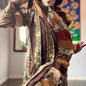 May include: A patchwork hooded jacket in shades of brown, tan, and cream, featuring various patterns like paisley, animal print, and stripes. The jacket is worn with a burgundy hat and a decorative mask with gold accents.