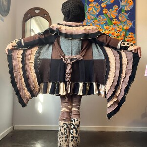 May include: A patchwork coat in brown, black, and tan with a ruffled design. The outfit includes matching leggings and leopard print boots. The person is seen from the back, with arms outstretched, showcasing the coat's design.