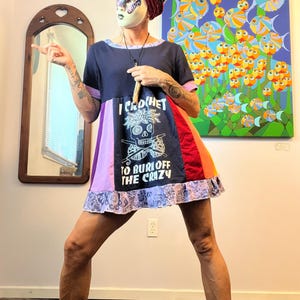 May include: A colorful patchwork dress with the text "I Crochet To Bury Off The Crazy" on the front. The dress features a skull design with crochet hooks. The dress has a navy blue top, purple, red, and orange panels, and a patterned hem.