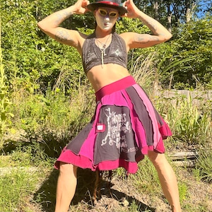 Könnte beinhalten: Eine Person trägt ein schwarzes Oberteil mit silbernem Paillettenmuster, einen rot-schwarzen Rock mit grafischem Druck und einen schwarzen Zylinder mit einer weißen Maske. Der Rock hat den Text "Morris" und "Preise 8,50 €" aufgedruckt.