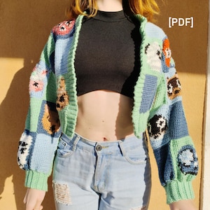 May include: A cropped cardigan with a patchwork design featuring various cartoon animals. The cardigan is made of a soft, blue, green, and white yarn. The cardigan is worn over a black mock neck shirt and blue jeans.