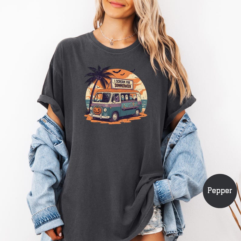 May include: Dark gray t-shirt with a graphic of a vintage van with a pumpkin face, palm tree, and the text "I Scream for Summerween." The van is teal and blue, set against a sunset backdrop. The shirt is a relaxed fit.