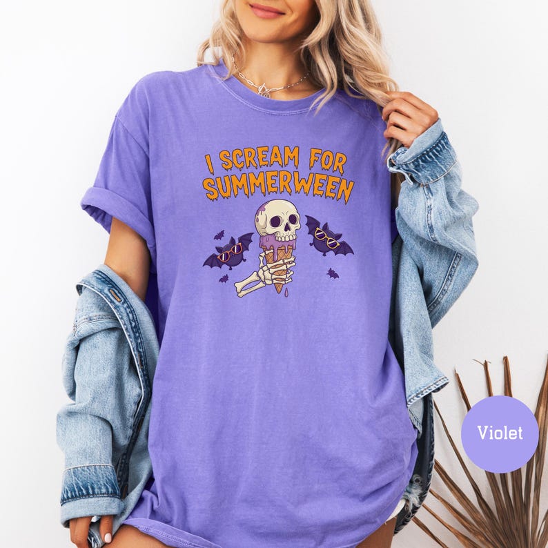 May include: Violet-colored t-shirt with the text "I SCREAM FOR SUMMERWEEN" in orange. The graphic features a skull holding an ice cream cone, with bats wearing sunglasses. A denim jacket is draped over the shoulders.