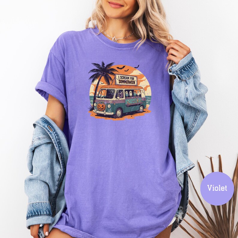 May include: Violet t-shirt with a graphic of a vintage van with a pumpkin face, palm tree, and the text "I Scream for Summerween." The van has ghosts in the windows. The background is a sunset over the ocean.