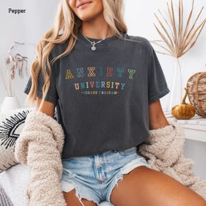 May include: A dark gray t-shirt with the text "Anxiety University - Honors Program" in rainbow colors.