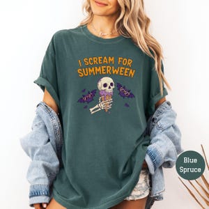 May include: A teal-colored t-shirt with the text "I SCREAM FOR SUMMERWEEN" in orange. The graphic features a skull with an ice cream cone, skeleton hands, and bats wearing sunglasses. The shirt is a relaxed fit.