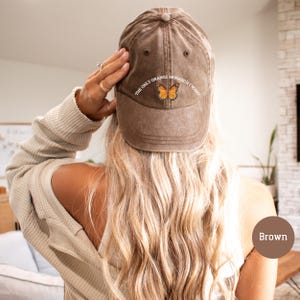 May include: Brown baseball cap with the text "THE ONLY ORANGE MONARCH I WANT" and a butterfly graphic. The cap is made of a soft, worn material.