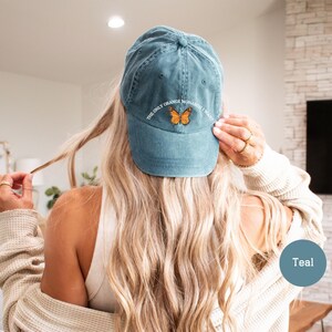 May include: Teal baseball cap with the text "THE ONLY ORANGE MONARCH I WANT" and a butterfly graphic. The cap is made of a soft material and has a curved brim. A casual accessory for everyday wear.