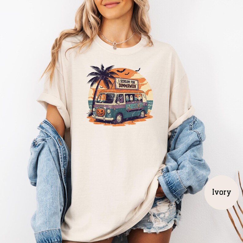 May include: Ivory-colored t-shirt featuring a graphic of a vintage van with a pumpkin face, palm tree, and the text "I Scream for Summerween." The van is teal and purple, with ghosts inside. The background shows a sunset and bats.