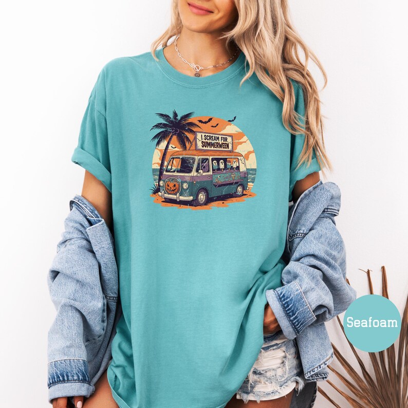 May include: Seafoam green t-shirt featuring a graphic of a vintage van with a pumpkin face, palm tree, and the text "I Scream for Summerween." The van has passengers and is set against a sunset backdrop.