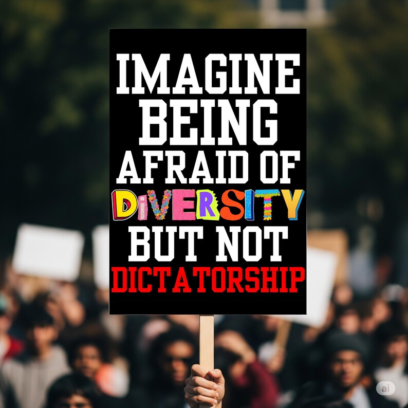 May include: A black sign with white text that reads "IMAGINE BEING AFRAID OF DIVERSITY BUT NOT DICTATORSHIP." The word "DIVERSITY" is in colorful letters. The sign is held up in a crowd of people.