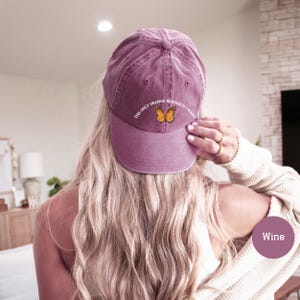 May include: A wine-colored baseball cap with the text "The Only Orange Monarch I Want" and a butterfly graphic. The cap is made of a soft, worn material.