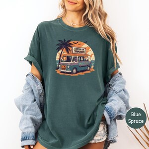 May include: Blue spruce t-shirt featuring a Halloween-themed graphic. The design includes a vintage van with a jack-o'-lantern, palm tree, and the text "I Scream for Summerween". The shirt has a relaxed fit.