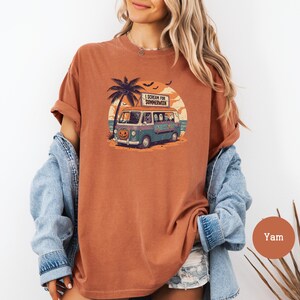 May include: A terracotta-colored t-shirt featuring a graphic of a van with ghosts, a pumpkin, and palm trees. The van has the text "I Scream for Summerween" on a sign. The design is set against a sunset backdrop with bats.