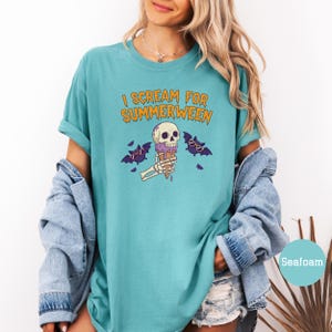 May include: Seafoam green t-shirt with the text "I Scream for Summerween" in orange. The graphic features a skull with sunglasses holding a purple ice cream cone, with bats on either side.