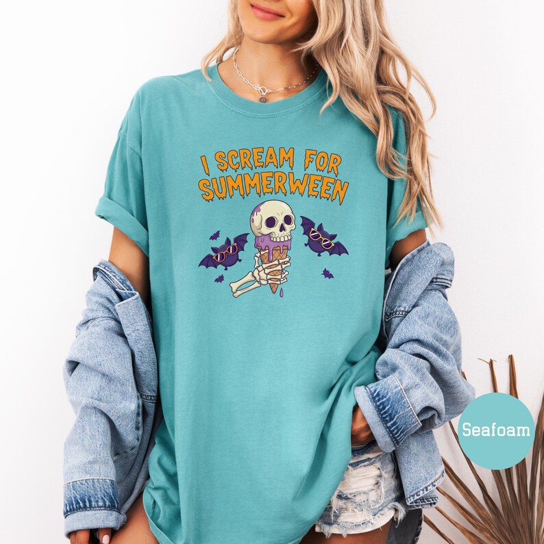 May include: Seafoam green t-shirt with the text "I Scream for Summerween" in orange. The graphic features a skull with sunglasses holding a purple ice cream cone, with bats on either side.