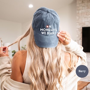 May include: Navy blue baseball cap with the text "ON MONDAYS WE MAHJ" in white. The cap has a curved brim and a distressed look. The cap is a classic six-panel design, perfect for casual wear.