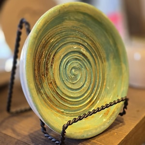 May include: A green and yellow ceramic dish with a spiral design. The dish is on a black metal stand.