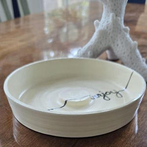 May include: White ceramic dish with a black line and the word "enjoy" written on it.