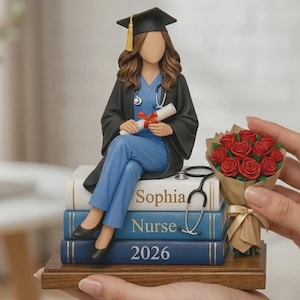 Puede incluir: Figura de una enfermera graduada con uniforme y toga, sentada sobre una pila de libros. Los libros están etiquetados como "Sophia", "Nurse" y "2026". También hay un estetoscopio y un ramo de rosas rojas.