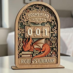 Peut inclure: Calendrier de bureau en bois avec le texte "BOOKS READ THIS YEAR" et "ROBIN'S LIBRARY". Le calendrier présente un dragon orange endormi, un compteur de livres affichant "001" et des éléments floraux décoratifs.