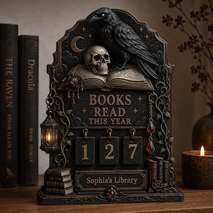 May include: A dark-toned decorative plaque featuring a black raven perched on an open book and a skull. The plaque displays the text "BOOKS READ THIS YEAR" above three hanging number tiles showing "127" and a nameplate reading "Sophia's Library".