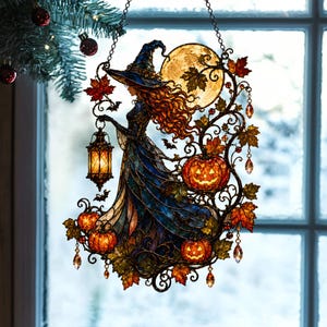 May include: A stained glass suncatcher featuring a witch in a blue hat and gown holding a glowing lantern. The design includes a large yellow moon, orange jack-o'-lanterns, autumn leaves, and small bats, all framed by intricate metal scrollwork.