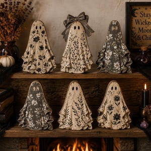 Peut inclure: Six figurines en forme de fantôme disposées sur une étagère en bois. Chaque fantôme présente un motif floral ou botanique unique en noir et blanc, avec deux découpes pour les yeux. Un fantôme est orné d'un grand nœud. Un cadre porte l'inscription Stay Wicked Moon Child.