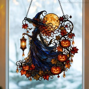 May include: A stained glass suncatcher featuring a witch in a blue dress and pointed hat holding a glowing lantern. The design includes a large yellow moon, orange jack-o'-lanterns, autumn leaves, and small bats, all suspended by a metal chain.