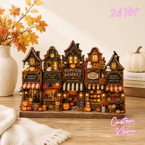 May include: A decorative miniature village display featuring five connected storefronts including a Pumpkin Market, Wicked Cider, Autumn Bakery, and Spooky Produce. The structure is illuminated with warm lights and adorned with pumpkins, ghosts, and black cats.
