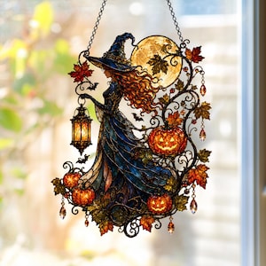 May include: A stained glass-style hanging suncatcher featuring a witch in a blue dress and pointed hat, holding a glowing lantern. The design includes a large yellow moon, orange jack-o'-lanterns, autumn leaves, and small bats, all suspended by a chain.