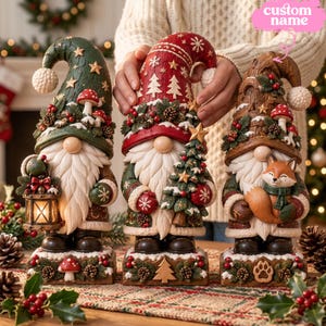 May include: Three decorative gnome figurines standing on rectangular bases. The left gnome wears a green hat with mushrooms and holds a lantern. The center gnome wears a red hat with trees and holds a tree. The right gnome wears a brown hat with a fox.