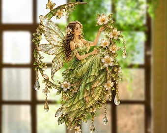 May include: A decorative hanging ornament featuring a fairy with translucent wings sitting on a crescent moon. The fairy wears a flowing green dress and is surrounded by white flowers, green leaves, and dangling clear crystal teardrop accents.