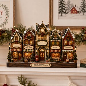 May include: A miniature Christmas village display featuring five connected buildings with illuminated windows, including a clock tower, bakery, and toy shop. The base features the text "MAKING MEMORIES, ONE CHRISTMAS AT A TIME" and the center building reads "THE CHRISTMAS MARKET EST 2019".