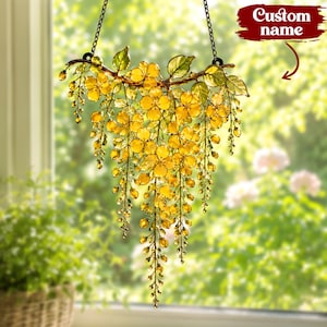 Op de afbeelding: Een hangende zonnevanger met een tros doorschijnende gele bloemen en groene bladeren, opgehangen aan een donkere metalen ketting. Het ontwerp bevat een takachtige structuur met trapsgewijze bloemelementen en een rood label met Custom name.